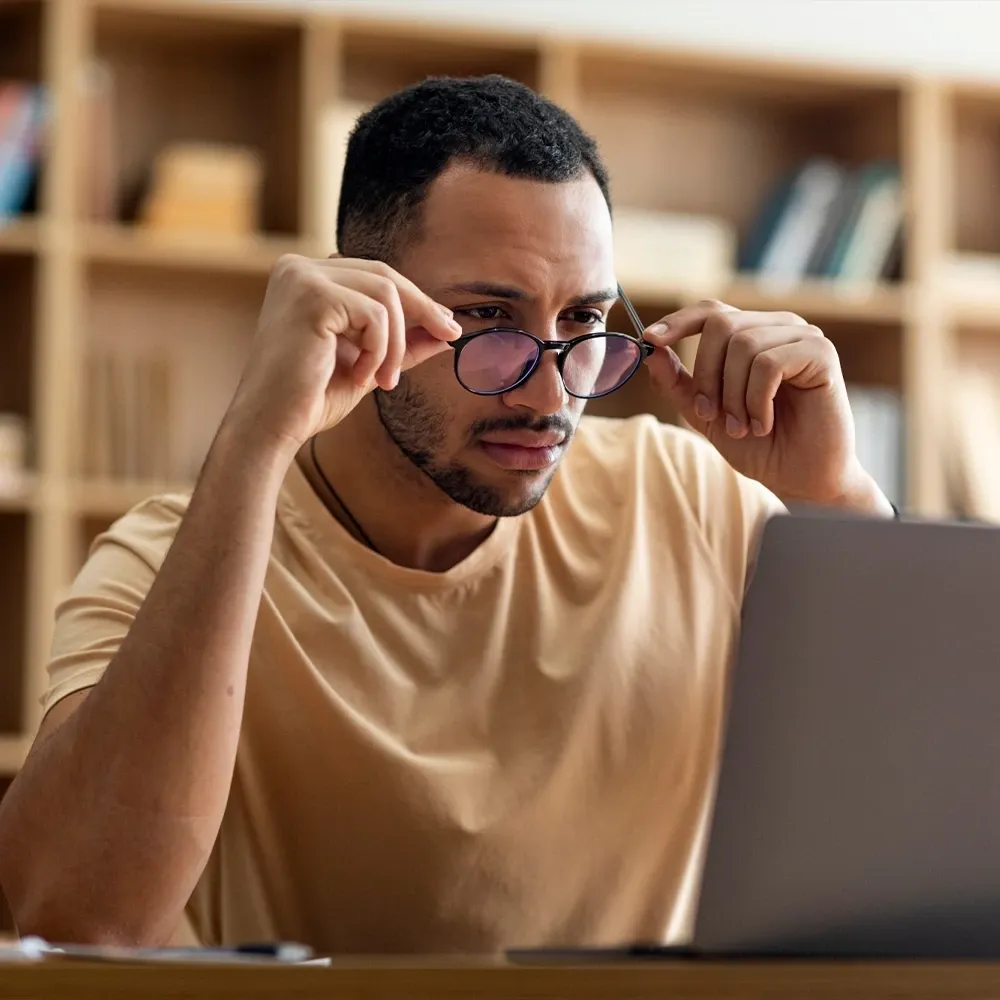 A man adjusting his glasses at a laptop